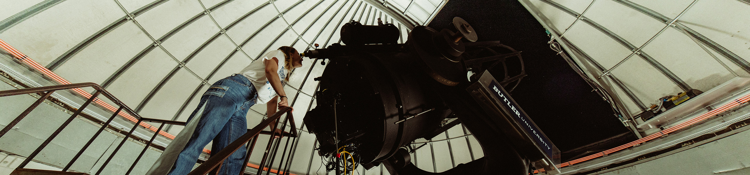 Female college student looks at night sky through large telescope in an observatory.