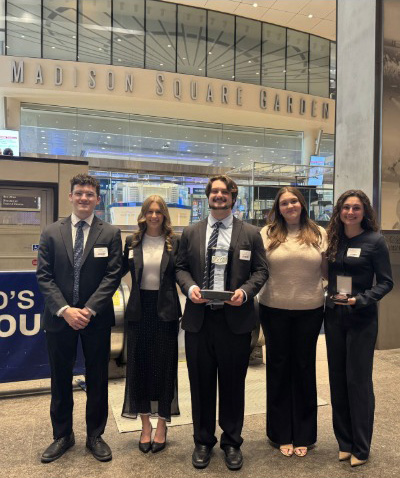 Group stands in front of Madison Square Garden holding awards.
