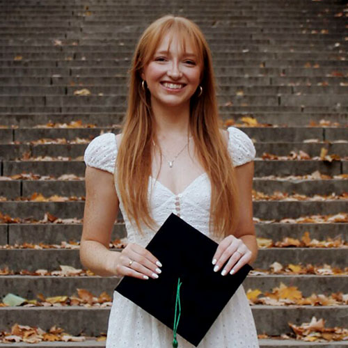 Jennah Worthington smiles in white dress while holding a black graduation cap.