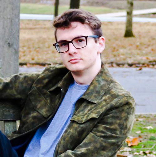 Luke Manship wears eyeglasses and a camoflauge jacket.