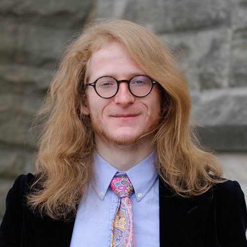 Alan Schneider smiles while in suit and tie and wearing round-frame eyeglasses.