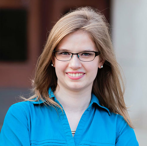 Hannah Stigter smiles in a blue collared shirt while wearing eyeglasses