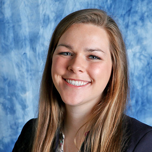 Jenna Wolf smiles while in front of a blue and white background.