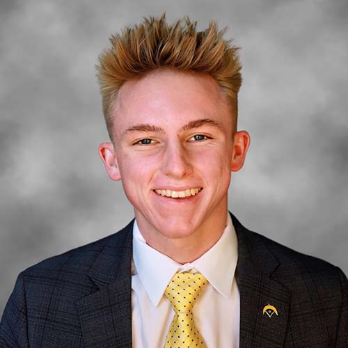 Nathan Marohn smiles while wearing a suit and yellow tie