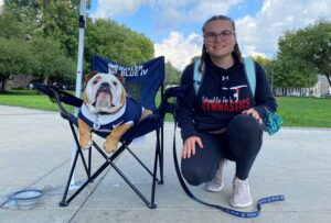 Student with backpack kneeling beside Butler Blue IV bulldog on a chair.