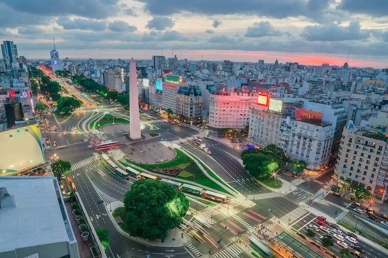Aerial time-lapse view of traffic along a primary thoroughfare with an obelisk in the center in Buenos Aires, Argentina, with city buildings receding into the background for miles.