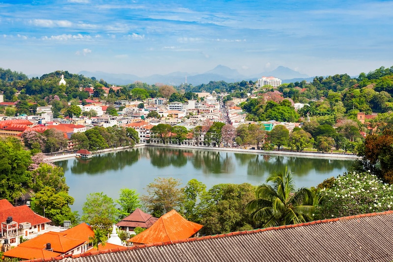 Lake surrounded by orange-roofed buildings in a hilly terrain of Kandy in Sri Lanka.