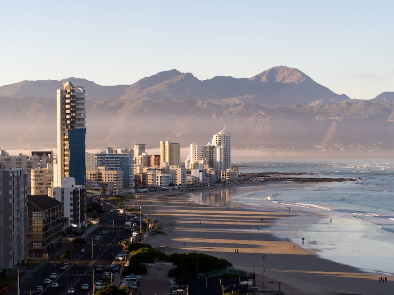 Beachfront view of waves and downtown skyline with large mountain ridges in the near distance.