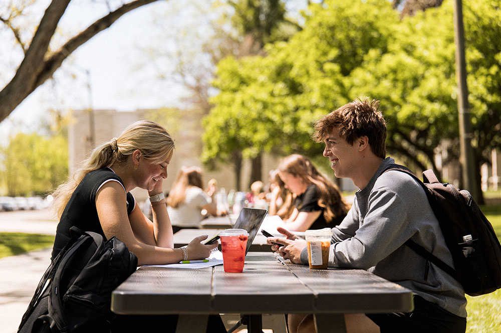 College students have conversations at tables outdoors.