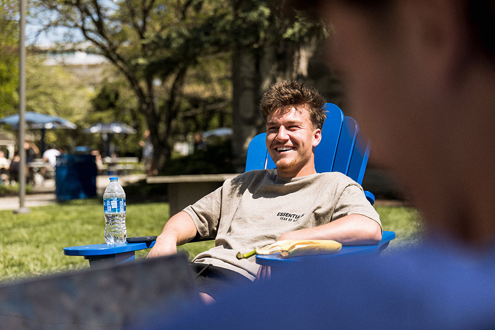Student in lounge chair outside laughing with others.