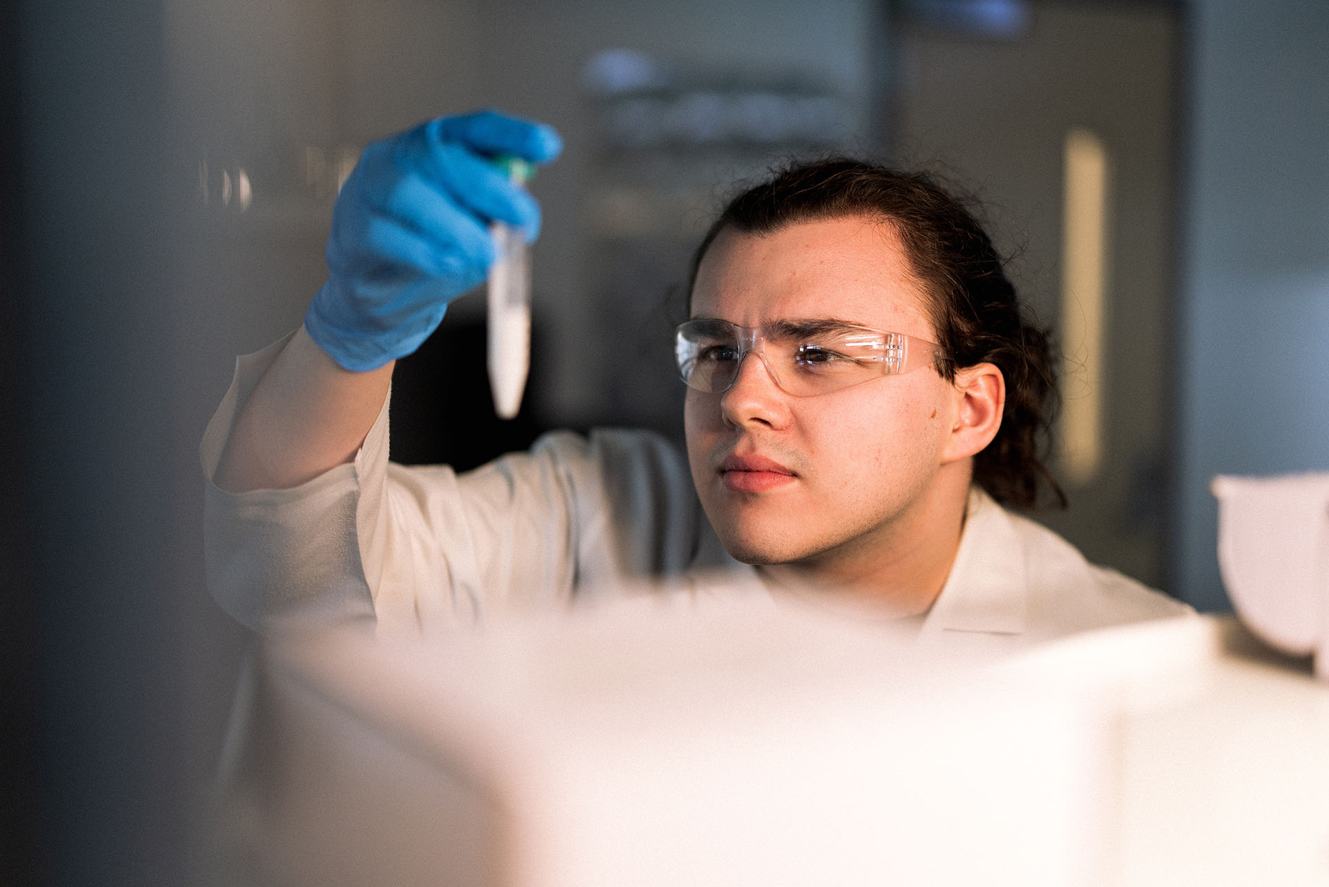 Chemistry student wearing lab glasses inspects a vial in the lab.