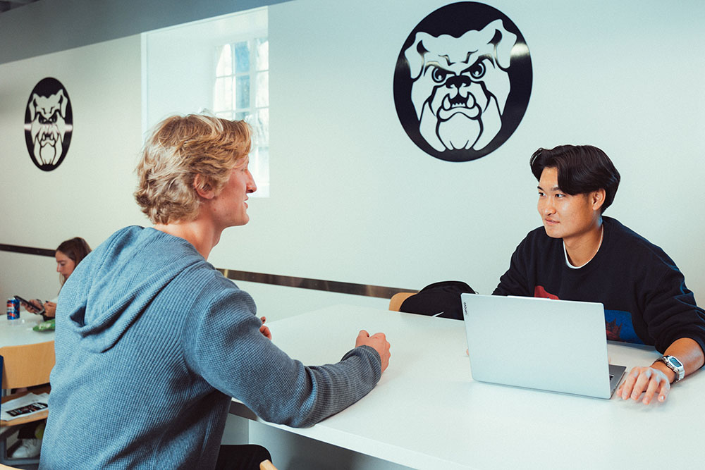 Two male students chat at a table in a cafeteria.