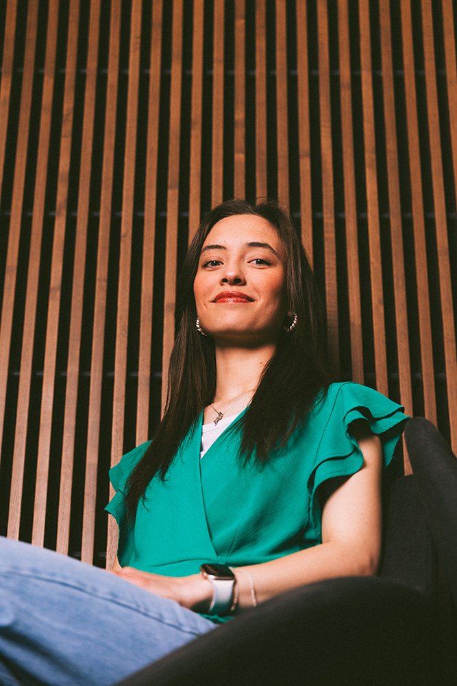 Portrait of Juanita Rojas as she sits in a chair with slats in the walls behind her.