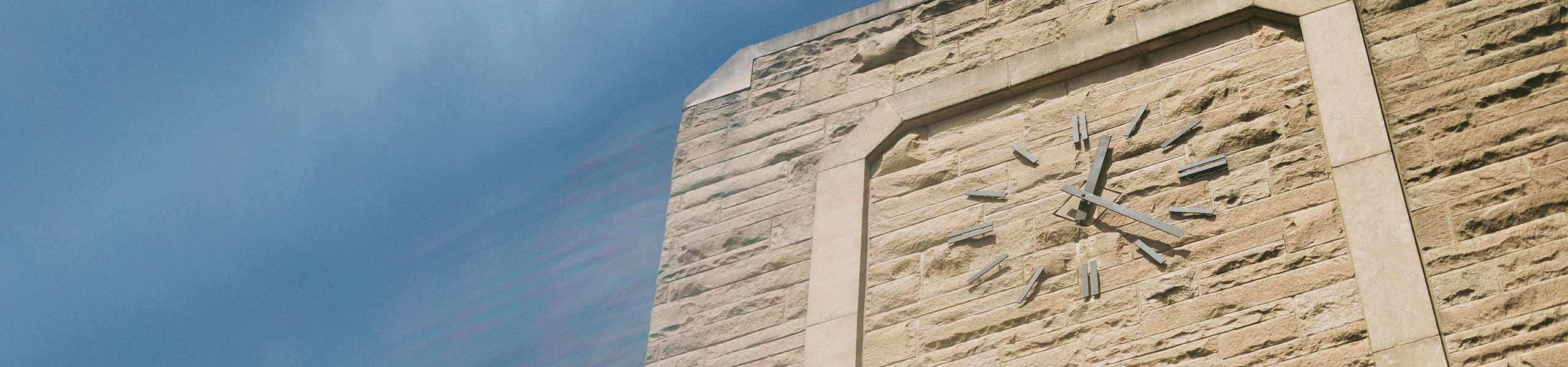 Clock on limestone face of Atherton Union with blue sky in background and a camera flare effect.