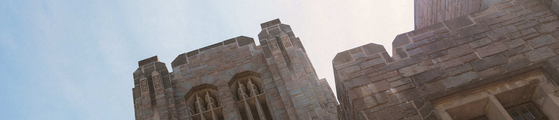 Tilted view of the top of Jordan Hall stone tower with sunshine overtop.