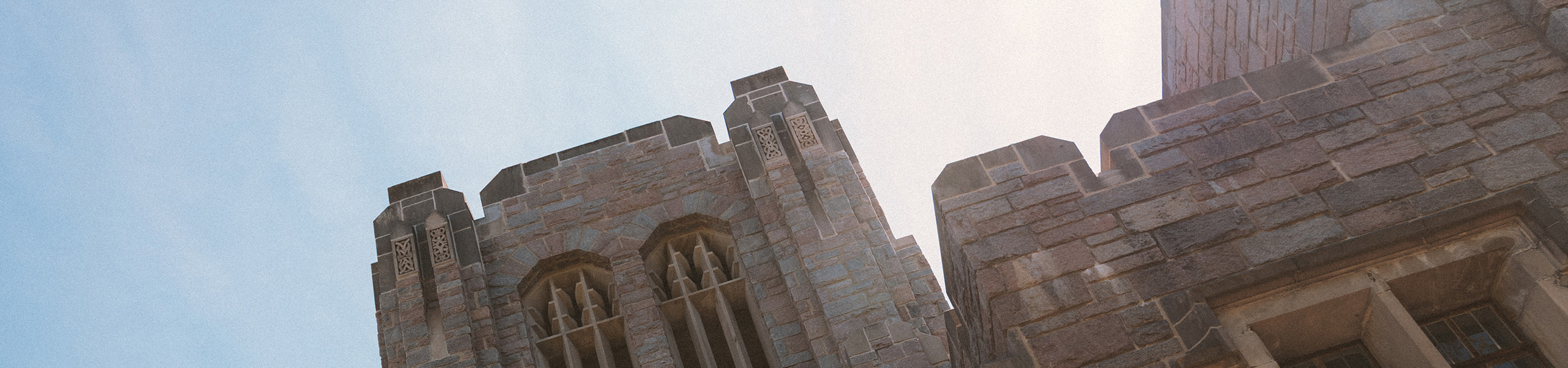 Tilted view of the top of Jordan Hall stone tower with sunshine overtop.