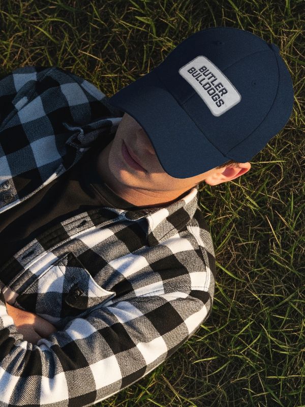 Butler Bulldog fan relaxing on the lawn in a branded blue hat and flannel shirt.